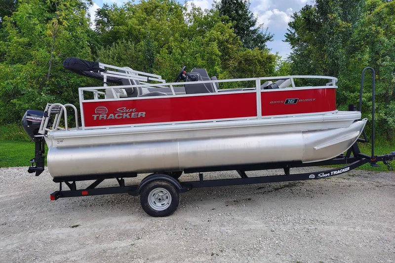 The Image of 2027 Sun Tracker Bass Buggy 16 XL Select pontoon boat on trailer, parked outdoors. - 0