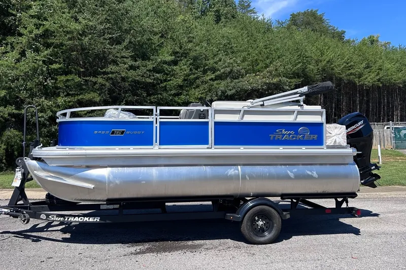 The Image of 2027 Sun Tracker Bass Buggy 16 XL Select pontoon boat on trailer, parked outdoors. - 0