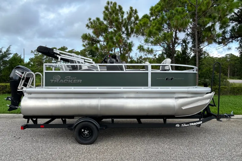The Image of 2027 Sun Tracker Bass Buggy 16 XL Select pontoon boat on trailer, parked outdoors. - 0