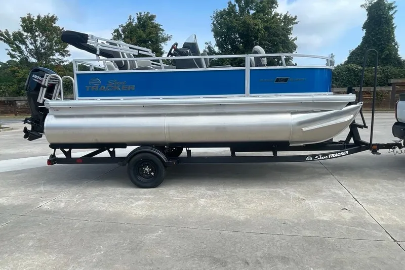 The Image of 2027 Sun Tracker Bass Buggy 16 XL Select pontoon boat on trailer, parked outdoors. - 0