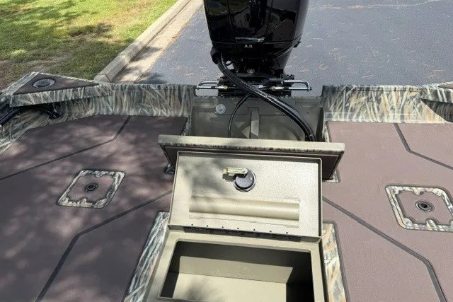 Slide: The Image of 2027 Tracker Grizzly 2072 CC boat with open storage compartment and motor, parked on pavement. - 15