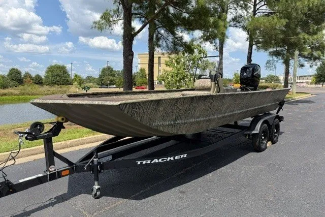 The Image of 2027 Tracker Grizzly 2072 CC boat on trailer, parked outdoors near trees and water. - 0