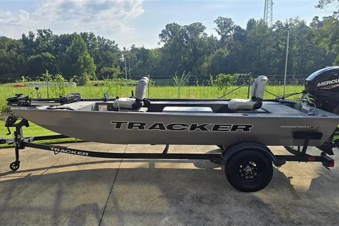 The Image of 2027 Tracker Panfish 17 boat on trailer, parked outdoors, with lush greenery in the background. - 0