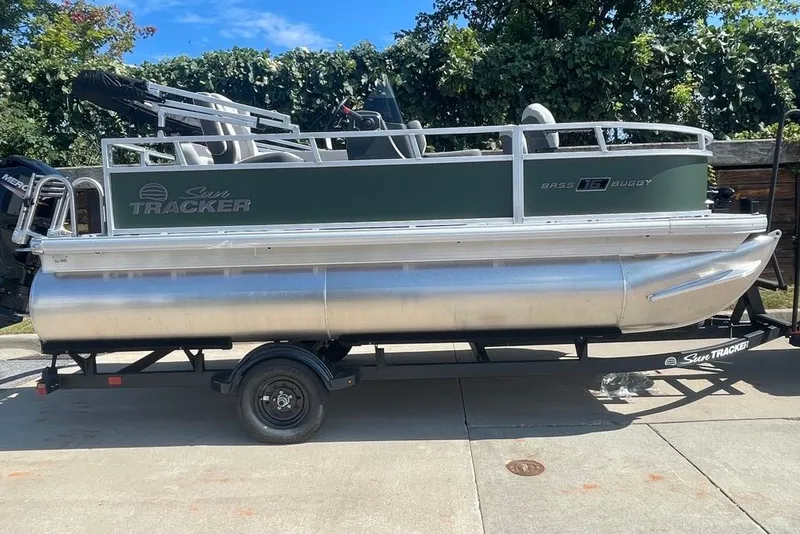 The Image of 2027 Sun Tracker Bass Buggy 16 XL Select pontoon boat on trailer, parked outdoors. - 0