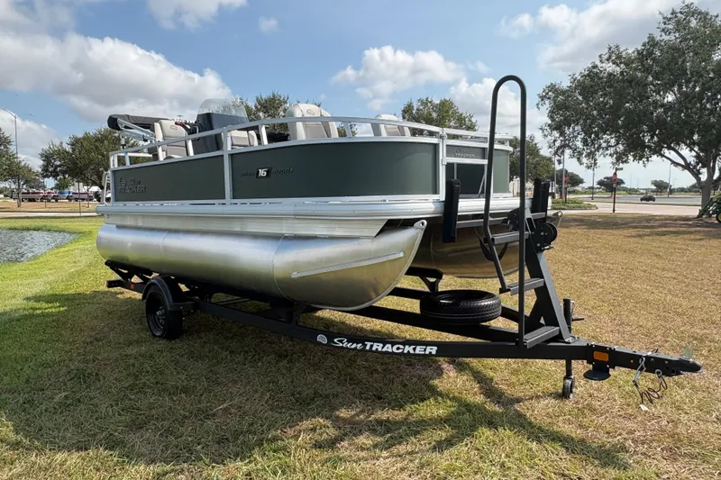 Slide: The Image of 2027 Sun Tracker Bass Buggy 16 XL Select pontoon boat on trailer, parked on grass. - 64