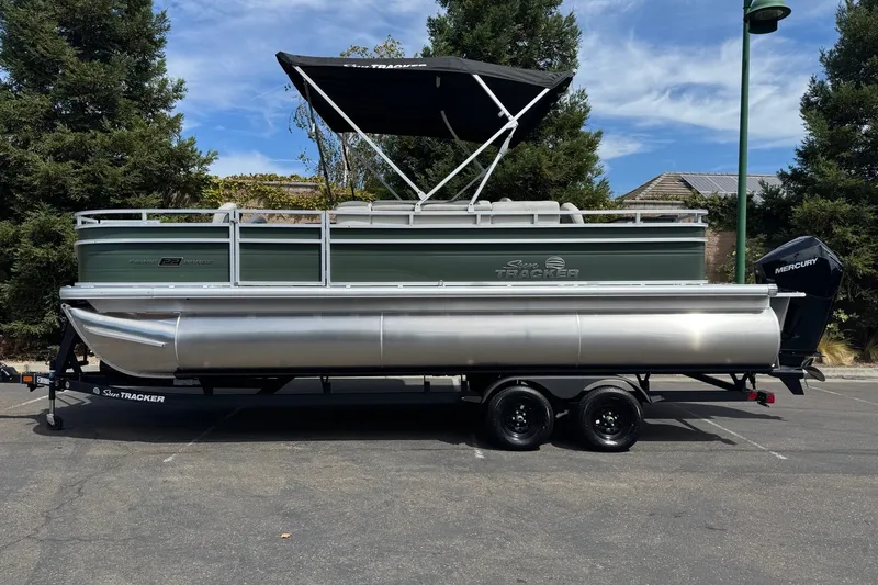 The Image of 2027 Sun Tracker Fishin' Barge 22 XP3 pontoon boat on trailer, parked outdoors. - 0