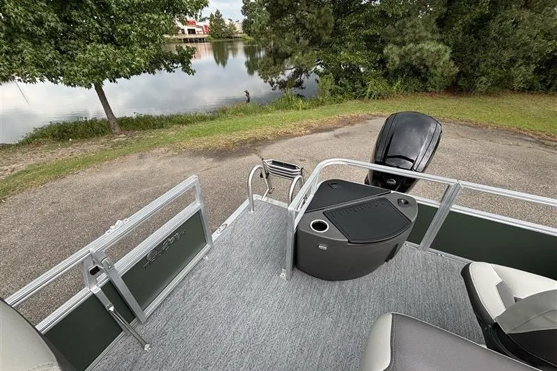 Slide: The Image of 2027 Sun Tracker Bass Buggy 18 DLX pontoon boat near a serene lake. - 26