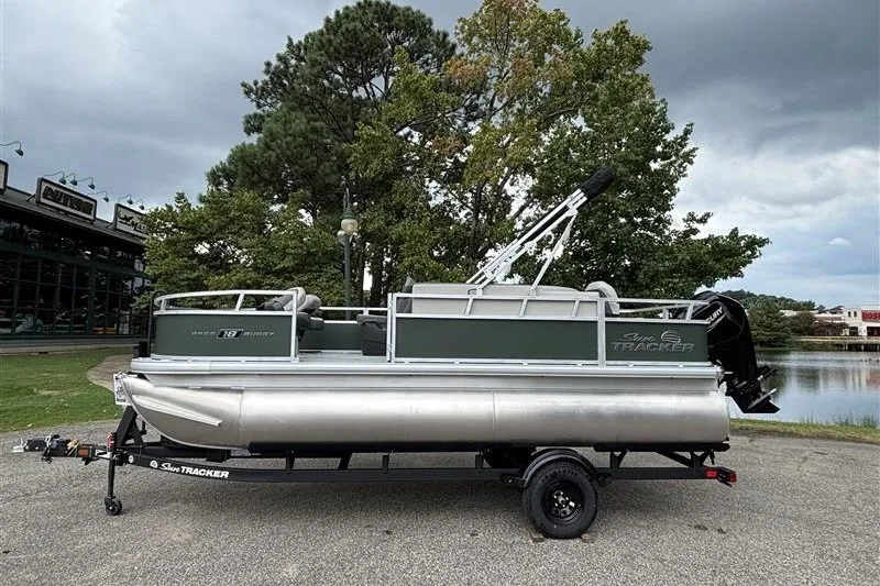 The Image of 2027 Sun Tracker Bass Buggy 18 DLX pontoon boat on trailer, parked near a lake. - 1