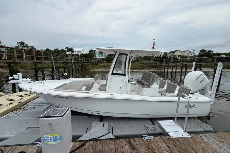 Slide: The Image of 2025 Sea Hunt BX25FS boat docked by a wooden pier on a calm river. - 2