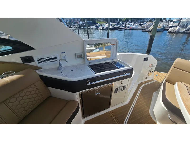 Slide: The Image of The 2026 Sea Ray Sundancer 320 Coupe Outboard features a sleek outdoor kitchen with a sink and grill. - 24