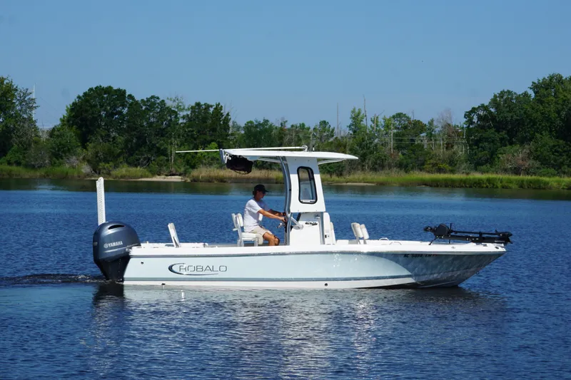 The Image of 2019 Robalo 226 Cayman boat cruising on a calm lake with lush green shoreline. - 1