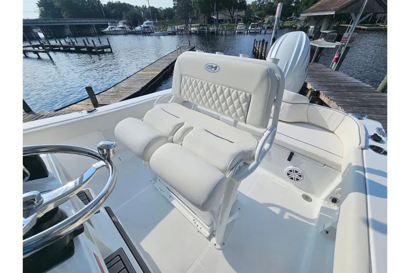 Slide: The Image of 2027 Sea Hunt Ultra 219 boat interior with white seating and steering wheel, docked by a marina. - 16