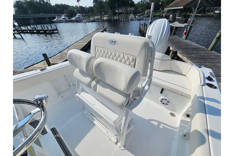 Slide: The Image of 2027 Sea Hunt Ultra 219 boat interior with white seating, docked by a scenic waterfront. - 15