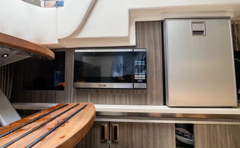 Slide: The Image of The galley of the 2024 Sea Ray Sundancer 320 Outboard features a microwave and a refrigerator. - 17