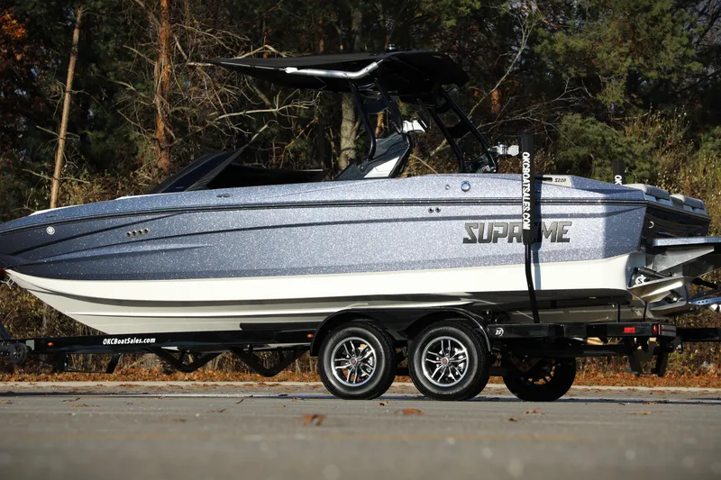Slide: The Image of 2026 Supreme S220 boat on trailer, parked outdoors with forest background. - 11