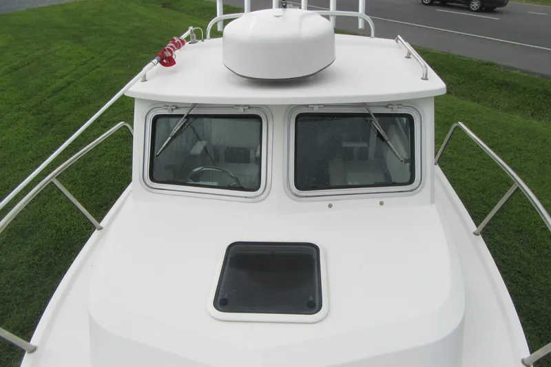 Slide: The Image of 2016 Parker 2120 Sport Cabin boat with white cabin and windshield, parked on grass. - 18