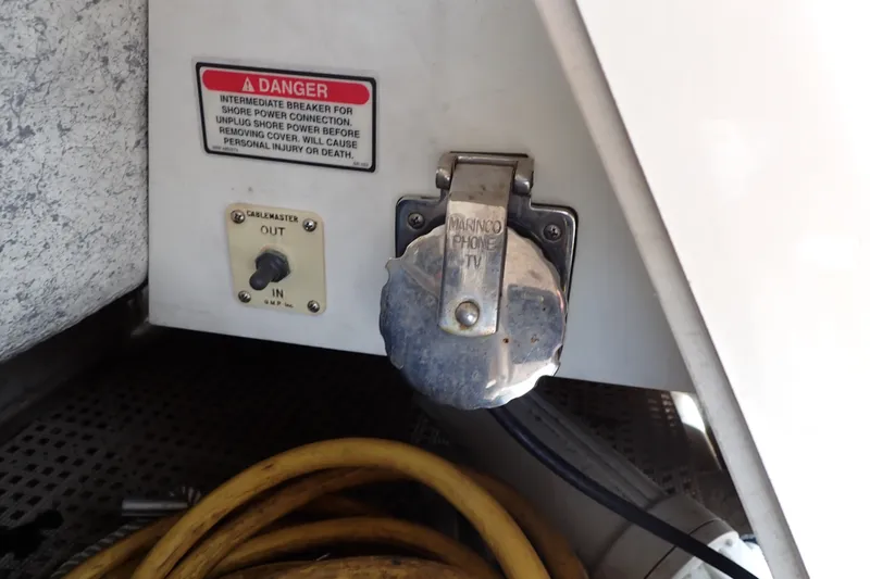 Slide: The Image of 1998 Sea Ray 480 Sedan Bridge power connection panel with warning label and cable storage. - 88