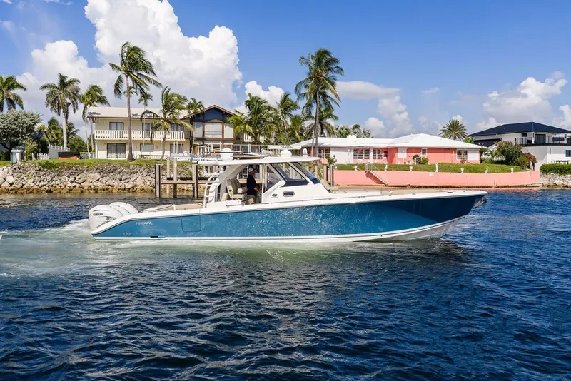 Slide: The Image of 2020 Pursuit S 408 Sport boat cruising near waterfront homes, under a clear blue sky. - 13