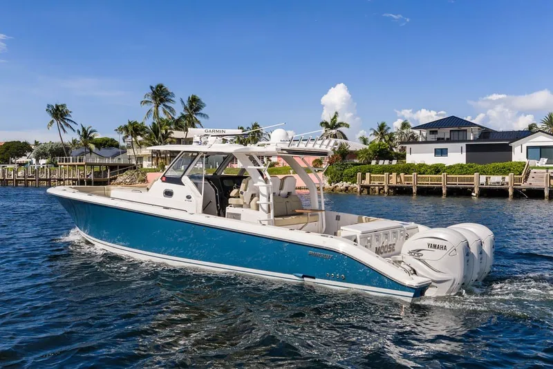 Slide: The Image of 2020 Pursuit S 408 Sport boat cruising near waterfront homes under a clear blue sky. - 10
