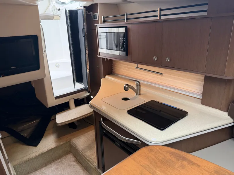 Slide: The Image of The interior of a 2014 Sea Ray Sundancer 280 features a compact kitchen with a sink, stove, and microwave. The space is modern and functional. - 33