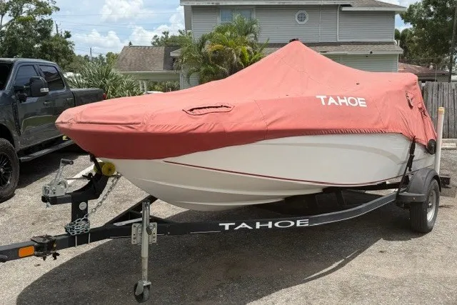 Slide: The Image of 2021 Tahoe T16 boat with red cover on trailer, parked in driveway. - 2