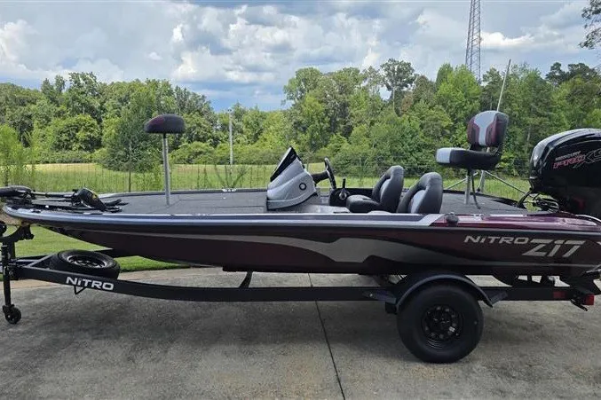 The Image of 2027 Nitro Z17 fishing boat on trailer, parked outdoors with lush greenery background. - 0