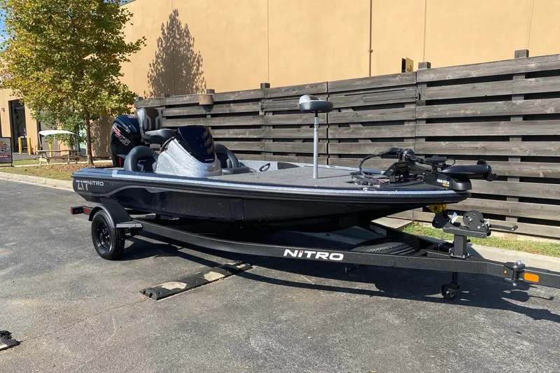 Slide: The Image of 2027 Nitro Z17 fishing boat on trailer, parked outdoors near wooden fence. - 2