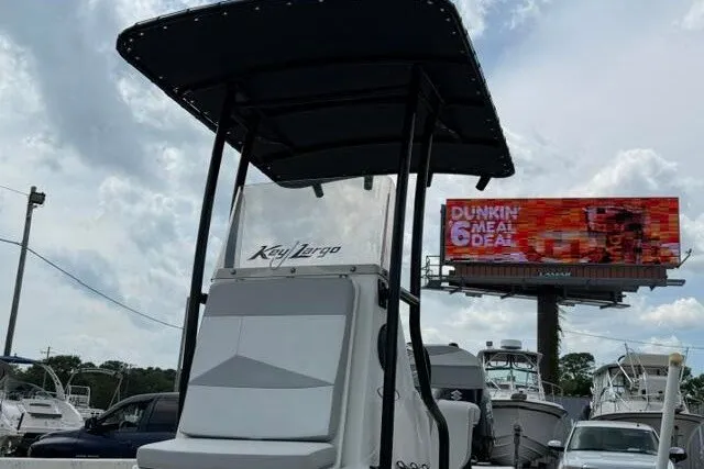 Slide: The Image of 2018 Key Largo 220 Bay boat with T-top, parked near other boats and a billboard. - 3