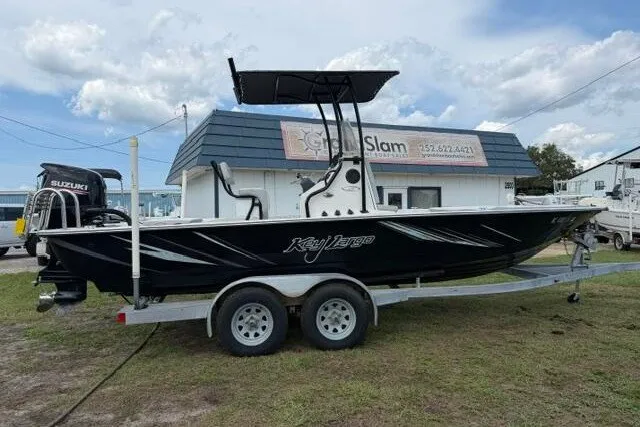Slide: The Image of 2018 Key Largo 220 Bay boat on trailer, parked near a building under a cloudy sky. - 8