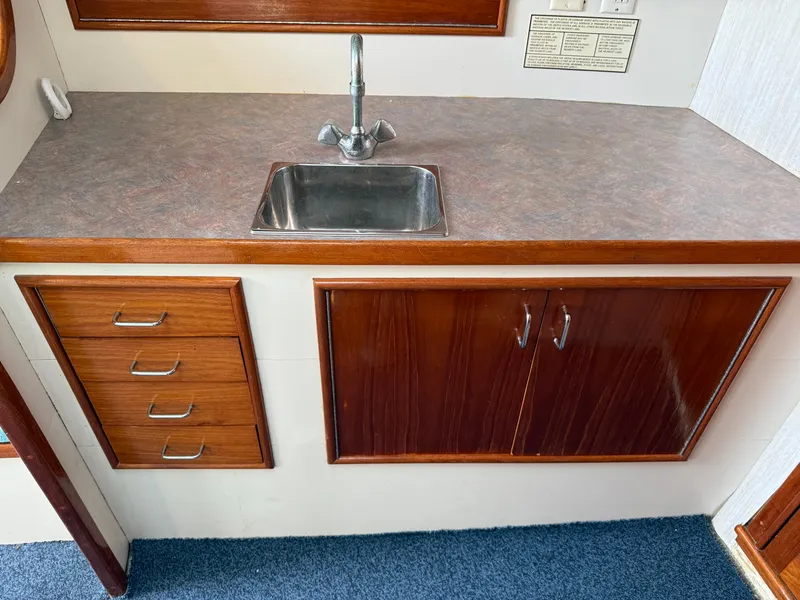 Slide: The Image of A kitchenette with a sink, wooden cabinets, and drawers inside a boat. - 37