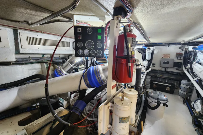 Slide: The Image of Engine room of a 1999 Hatteras 65 Convertible yacht, featuring control panel and fire extinguisher. - 73