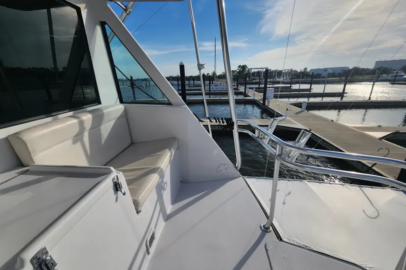 Slide: The Image of 1999 Hatteras 65 Convertible yacht at marina, featuring cushioned seating and stainless steel railings. - 50