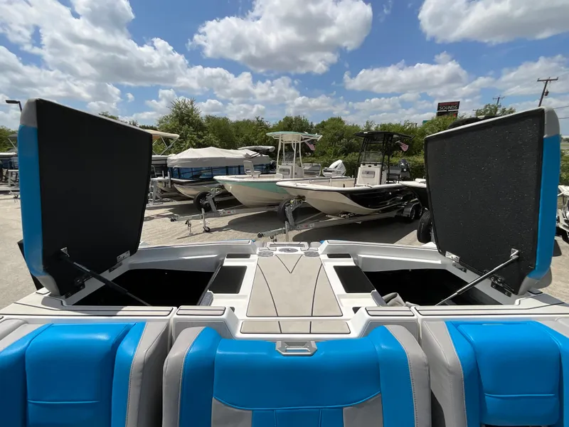Slide: The Image of The image shows the rear of a 2022 Malibu 23LVS boat with blue and gray seats. Storage compartments are open, and other boats are visible in the background. - 12