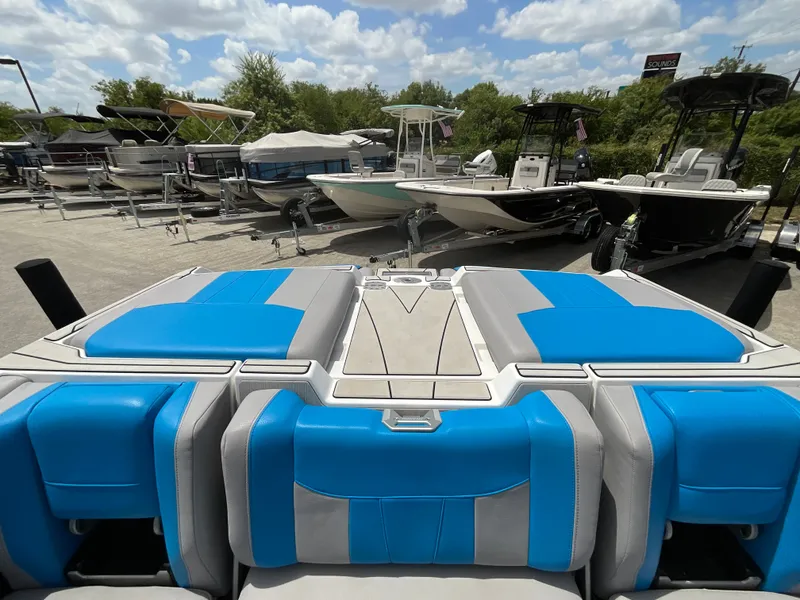 Slide: The Image of The image shows the stern of a 2022 Malibu 23LVS boat with blue and gray upholstery. Other boats are visible in the background on a lot. - 11