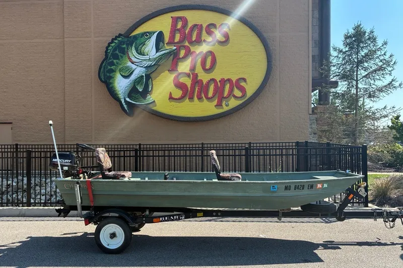 The Image of A 1999 green Jon Boat on a trailer in front of a Bass Pro Shops building. - 1