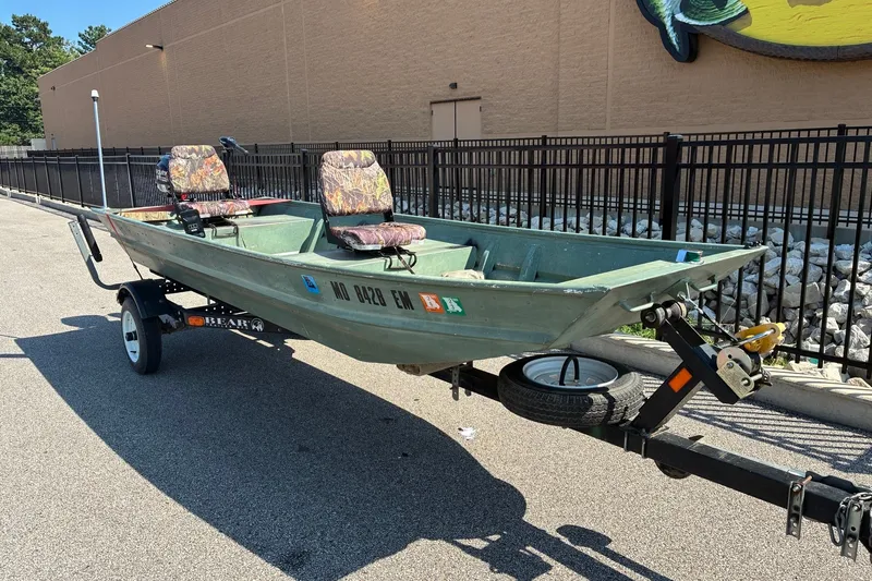 Slide: The Image of 1999 Jon Boat 1436 on trailer with two camo seats, parked outdoors. - 5