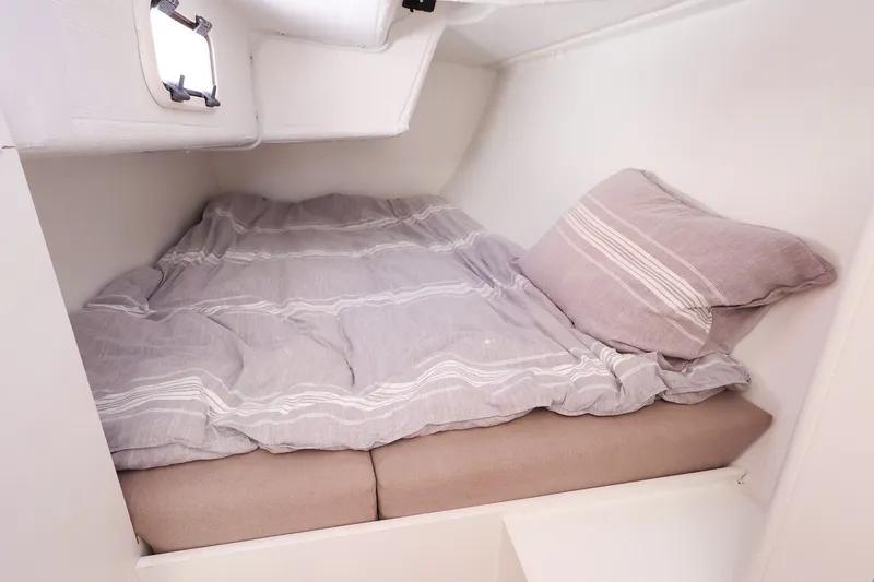 Slide: The Image of Cozy cabin bed in 2023 J Boats J/99 sailboat, featuring striped bedding and a small window. - 59