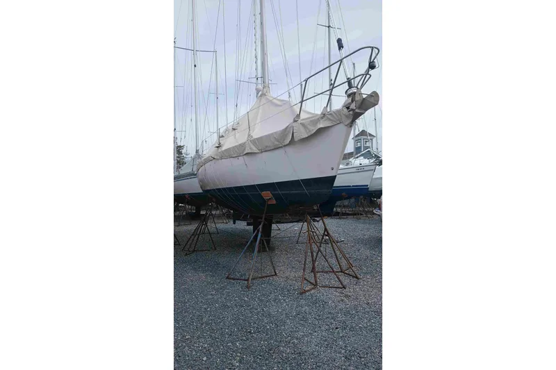 Slide: The Image of 1990 Canadian Sailcraft 34 sailboat on stands, covered, in a gravel boatyard. - 27