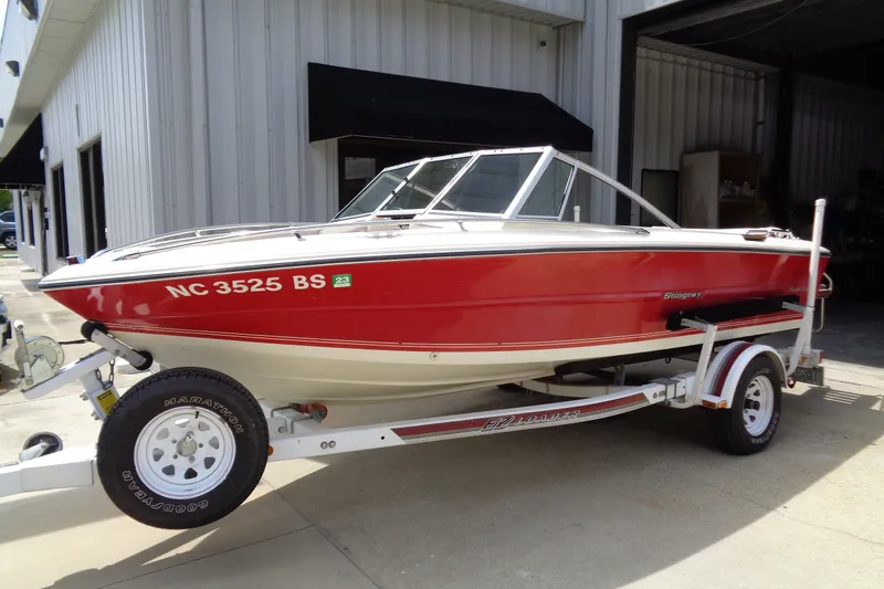 The Image of 1989 Stingray 172 SC boat on trailer, red and white, parked outside a building. - 1