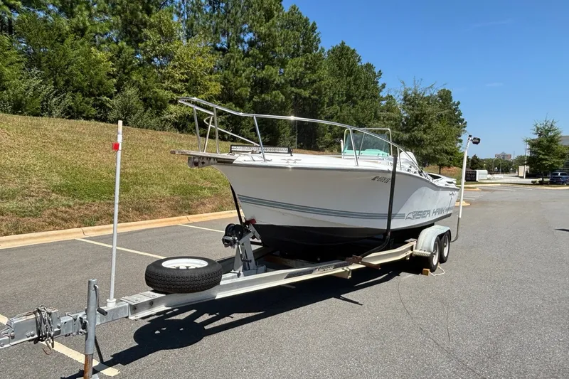 Slide: The Image of 1989 Chris-Craft 213 Sea Hawk boat on trailer in parking lot, surrounded by trees. - 14