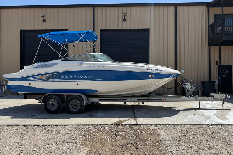 Slide: The Image of 2009 Rinker 248 Captiva Deckboat on trailer, blue and white, parked outside a building. - 1