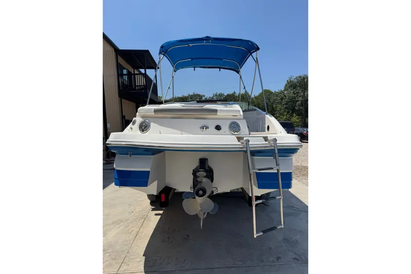 Slide: The Image of 2009 Rinker 248 Captiva Deckboat with blue canopy and ladder, parked outdoors. - 19