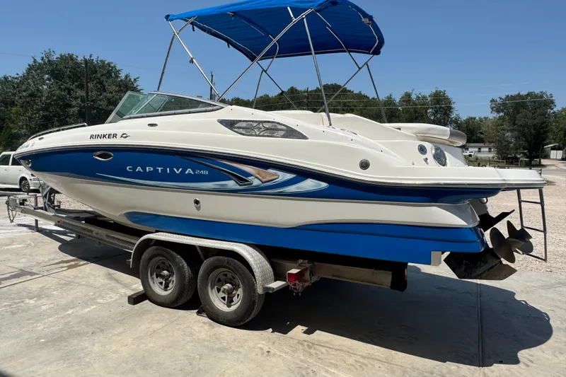 Slide: The Image of 2009 Rinker 248 Captiva Deckboat on trailer with blue canopy, parked outdoors. - 18