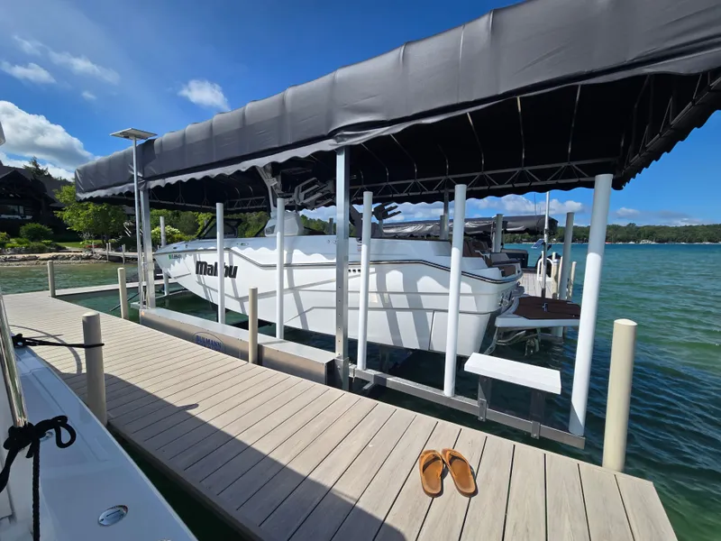 Slide: The Image of A white 2024 Malibu M242 boat is docked under a black canopy on a wooden pier. - 1