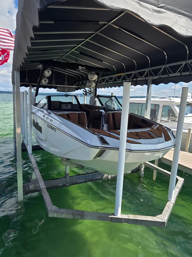 Slide: The Image of A white 2024 Malibu M242 boat is on a lift above clear water. - 6