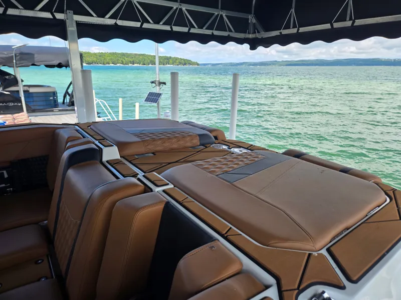 Slide: The Image of The image shows the rear of a 2024 Malibu M242 boat with brown seats and a lake in the background. - 2