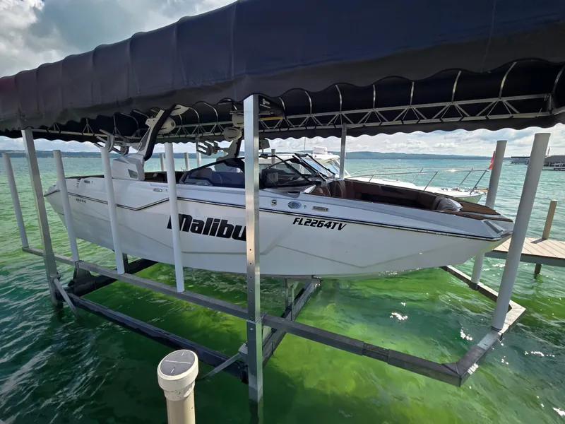The Image of A white 2024 Malibu M242 boat on a lift above green water. - 0