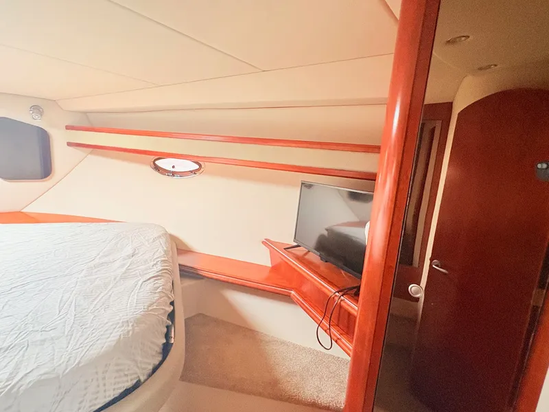 Slide: The Image of The cabin of a 2007 Cruisers 37O Express with a bed, TV, and wood accents. - 27
