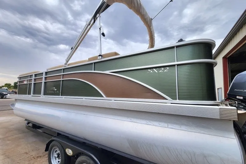 Slide: The Image of 2018 Bennington SSX21 pontoon boat with green and brown exterior, parked on a trailer. - 2
