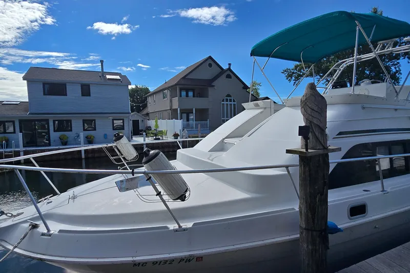 The Image of 1995 Mainship 31 Sedan Bridge docked near waterfront homes under a clear blue sky. - 0